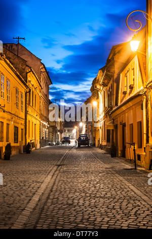 Brasov, Transylvania. Nachtaufnahme des Mittelalters gepflasterte Strasse in der Innenstadt der Stadt. Sächsischer Meilenstein in Rumänien. Stockfoto