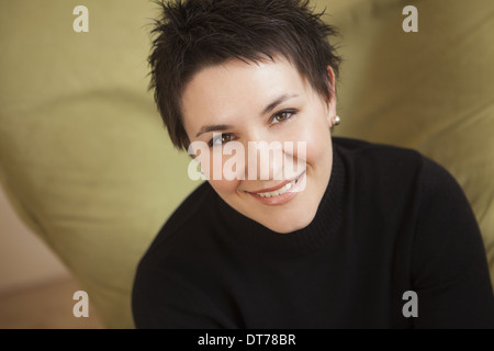 Eine Frau mit kurzen stacheligen braunen Haaren, trägt einen schwarzen Rollkragenpullover. Lächelnd und blickte. Stockfoto