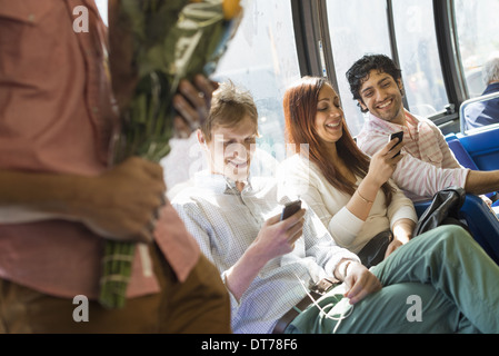 Männer und Frauen auf einem Stadtbus in New York City. Zwei Personen überprüfen ihre Telefone Blüten. Stockfoto