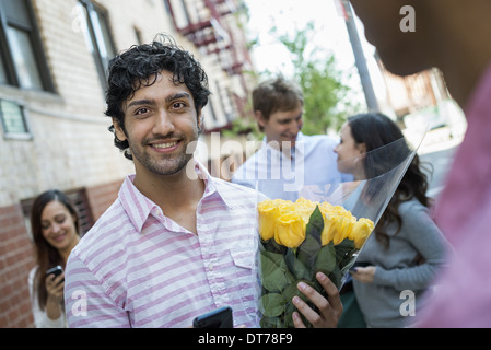 New York City Street. Eine Gruppe von fünf Personen, ein Mann mit einem Blumenstrauß und einer Frau, die ihr Handy überprüfen. Stockfoto