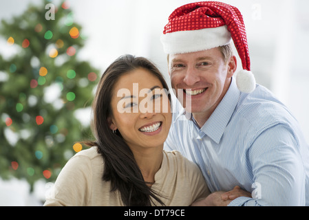 Ein Mann in eine Weihnachtsmann-Mütze. Zuhause. Ein geschmückter Weihnachtsbaum.