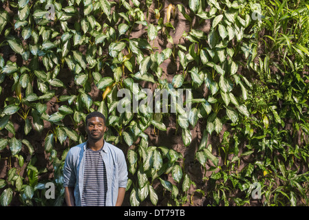 Ein Mann steht vor einer Wand bedeckt in Kletterpflanzen und Efeu. Stockfoto
