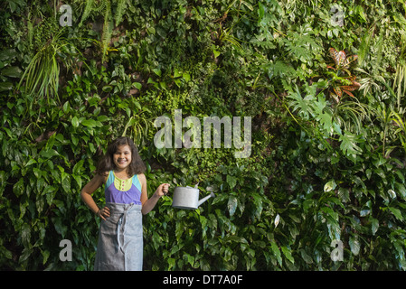 Ein junges Mädchen stand vor einer Wand mit Farnen bedeckt und Kletterpflanzen. Stockfoto