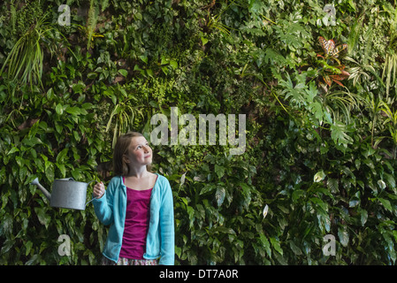 Ein junges Mädchen stand vor einer Wand mit Farnen bedeckt und Kletterpflanzen. Stockfoto