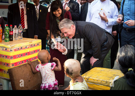 Yangon, Myanmar. 11. Februar 2014. HANDOUT - zeigt ein Handout Bild Bundespräsident Joachim Gauck zuerst ein kleines Mädchen, dessen Schwester ihr Haar an der Bordsteinkante in Yangon, Myanmar, 11. Februar 2014 geschnitten hat. Gauck ist auf eine viertägige Staatsbesuch in Myanmar. Foto: Bundesregierung/Guido Bergmann/Dpa (-. MANDATRORY CREDIT: BUNDESREGIERUNG/GUIDO BERGMANN/DPA) / Dpa/Alamy Live News Stockfoto