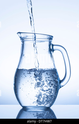 Fließendes Wasser in einen Krug auf blauem Hintergrund Stockfoto