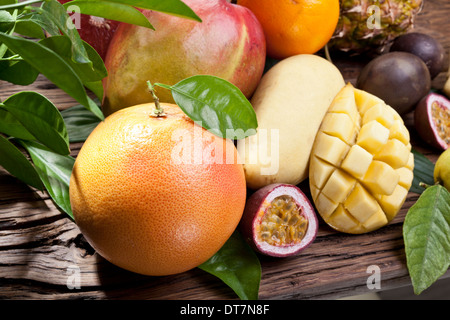 Exotische Früchte auf einem Holztisch mit dunkelgrünem Laub auf dem Hintergrund. Stockfoto