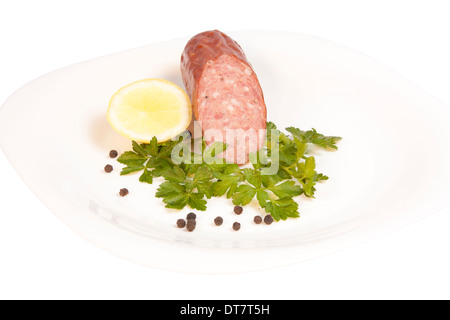 Salami mit Petersilie, Zitrone und Pfeffer auf einem Teller isoliert auf weißem Hintergrund mit Beschneidungspfad Stockfoto