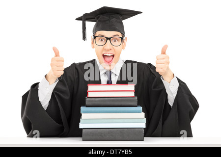 Männliche Studentin sitzt hinter Stapel Bücher und geben Daumen hoch Stockfoto