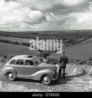 Historisches Bild von der 1950er Jahre zeigt einen Mann, der neben seinem geparkten Auto, bewundern Sie die Aussicht auf die Landschaft und die Felder. Stockfoto