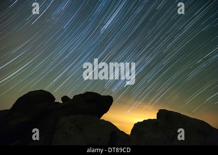 Lichtverschmutzung erhellt den Himmel und die Sterne Tails über große Felsbrocken. Stockfoto