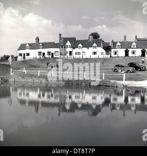 Historisches Bild von der 1950er Jahre zeigen eine Reihe von Hütten auf einem Hügel über einem Dorfteich, England. Stockfoto