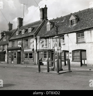 Historisches Bild von der 1950er Jahre zeigt eine alte Wasser gut und Markt Kreuz in der Mitte eine Dorfstraße, England. Stockfoto