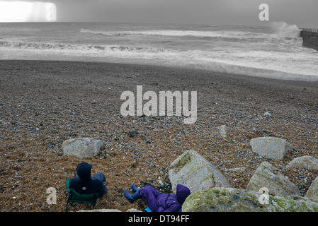 Paar sitzt am Strand beobachten die stürmische See, Hastings UK Stockfoto