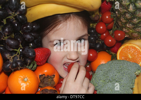 Kaukasische Mädchen Gesicht umgeben von Obst und Gemüse Essen eines Apfels, fünf am Tag, England, UK Stockfoto