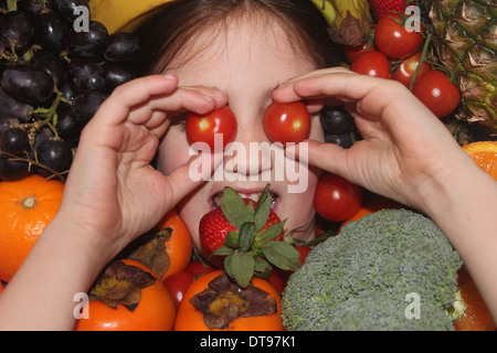 Kaukasische Mädchen Gesicht umgeben von Obst und Gemüse, fünf eine Tag, England, UK Stockfoto