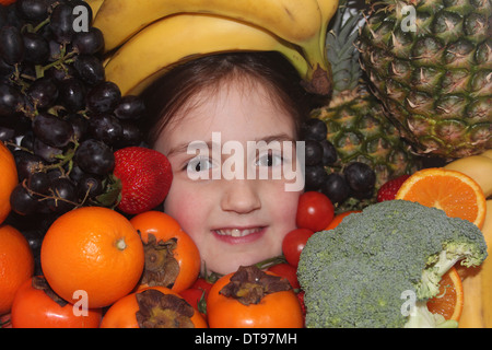 Kaukasische Mädchen Gesicht umgeben von Obst und Gemüse, fünf eine Tag, England, UK Stockfoto