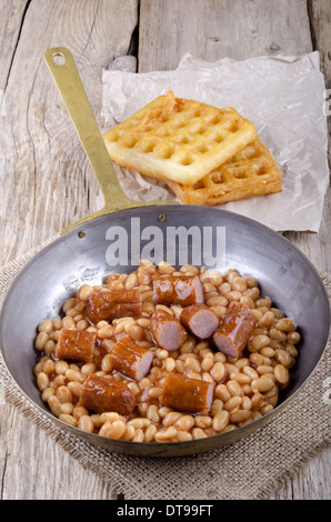 gebackene Bohnen mit Bratwurst und nach Hause gemachte Waffeln in einer Pfanne Stockfoto