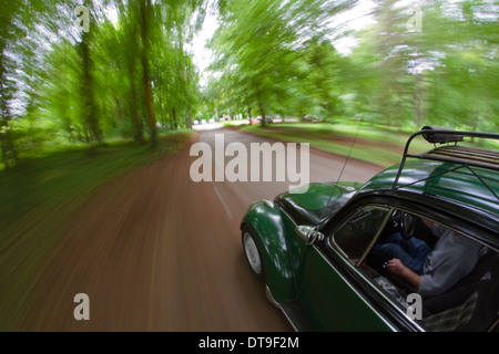 in einem klassischen luftgekühlten VW-Käfer mit einem Vintage Dachgepäckträger und zwei getönten Farbe einer bewaldeten Gasse fahren. Stockfoto