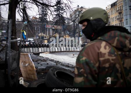 Kiew, Ukraine. 11. Februar 2014. Ein Anti-Regierungs-Demonstranten mit einem Helm und Armee Anzug an eine Barrikade im Zentrum von Kiew, wie Polizei Wache am 12. Februar 2014 stehen. Der Ukraine Unruhen brachen im November 2013, nachdem Präsident Viktor Yanukovych ein Assoziierungsabkommen mit der Europäischen Union für engere Beziehungen mit Moskau abgelehnt und die Turbulenzen ein all-out Bewegung inzwischen ist, ihn zu verdrängen. Russland die nächste Tranche seines Darlehens $ 15 Milliarden in die Ukraine am Ende des Monats veröffentlichen werden, sagte eine Zeitung in der Nähe von Präsident Viktor Yanukovych am 10. Februar, Anschluß an die Gespräche zwischen Stockfoto
