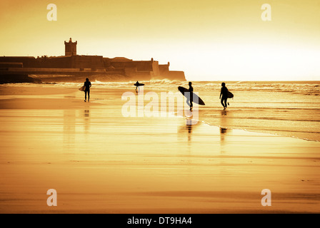 Silhouette der Surfer zu Fuß am Strand bei Sonnenuntergang Stockfoto