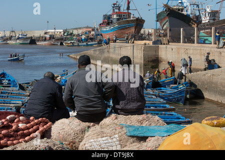 Drei Männer sitzen auf Fischernetze beobachten die blauen Fischerbooten der Fang anlanden Stockfoto