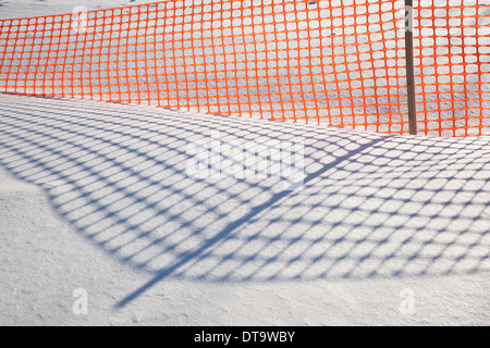Schatten von einem orange Kunststoff scHneeZaun machen Muster auf dem New England Schnee. Stockfoto