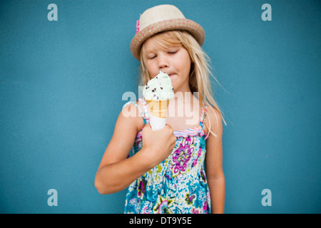 Süße junge Mädchen mit Vanille Eis außerhalb gegen blaue Wand Hintergrund Stockfoto