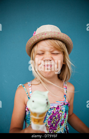 Süße junge Mädchen mit lustigen Ausdruck halten Eiswaffel außerhalb Hintergrund blaue Wand Stockfoto