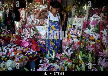 Manila, Philippinen. 13. Februar 2014. Ein Blume Lieferanten bindet ihre Schürze neben Blumensträußen zum Verkauf einen Tag vor Valentinstag auf dem Dangwa Blumenmarkt in Manila, Philippinen, 13. Februar 2014. Viele Blumenhändler haben beginnt mit dem Verkauf von Blumen und Rosen aus Anlass des Valentins Day.Photo: Ezra Acayan/NurPhoto Credit: Ezra Acayan/NurPhoto/ZUMAPRESS.com/Alamy Live News Stockfoto