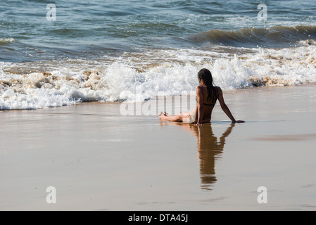 Eine junge Frau trägt Bikini sitzt im Sand von Anjuna Beach, Anjuna, Goa, Indien Stockfoto