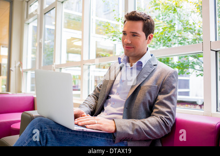 Hübscher junger Geschäftsmann arbeiten mit Laptop auf Sofa im Büro Stockfoto