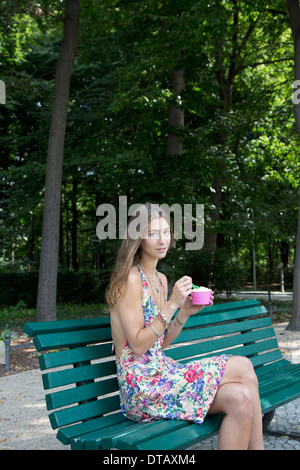 Junge Frau halten Eis sitzen auf der Parkbank, Porträt Stockfoto