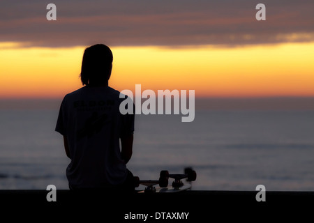 Ein junger Mann mit einer Pause von skateboarding und genießen Sie einen herrlichen Sonnenuntergang über der Nordsee, Katwijk Aan Zee, Südholland. Stockfoto