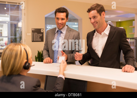 Geschäftsleute, die Kommunikation mit Frau Empfangsdame in Lobby, gibt sie eine Abzeichen Stockfoto
