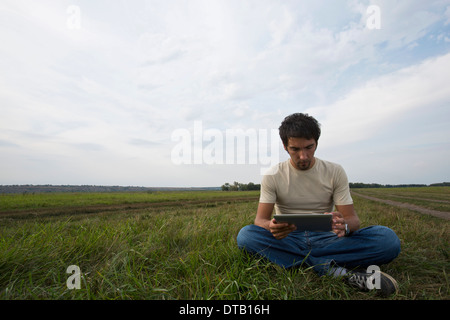 Junger Mann auf dem Rasen sitzen und mit digital-Tablette Stockfoto