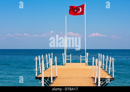 Kleine hölzerne Pier und rote Flagge winken mit dem Wind in Kemer - Urlaubsort am Mittelmeer in der Türkei. Stockfoto