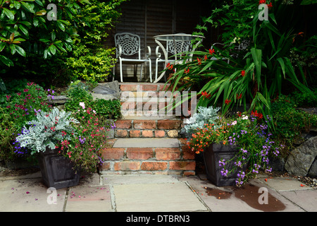 erhöhten Terrasse Sitzgelegenheiten Bereich rote Ziegel Schritte Container Container Gartenarbeit weißen Schmiedeeisen Sitz Sitze gemischte Pflanzung Schema Stockfoto