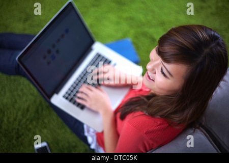 Junge Frau sitzt auf Teppich auf Laptop tippen Stockfoto