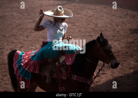 Ein Escaramuza begrüßt, als sie ihr Pferd reitet, bevor Sie im Wettbewerb mit einer Escaramuza in Lienzo Charros el Penon, Mexiko-Stadt Stockfoto