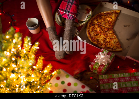 Junge Frau Beine unter Weihnachtsgeschenke und Pizza-Schachtel Stockfoto