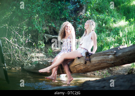 Zwei Mädchen im Teenageralter sitzen auf Baum in Waldbach