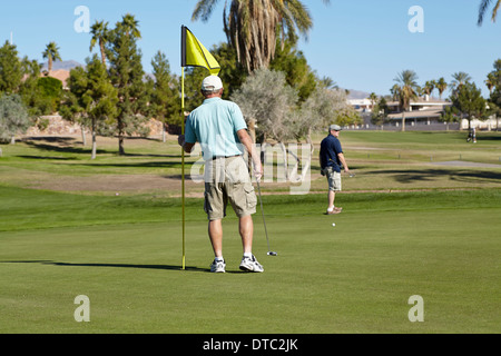 Zwei männliche Golfer auf dem Grün mit Fahne Stockfoto