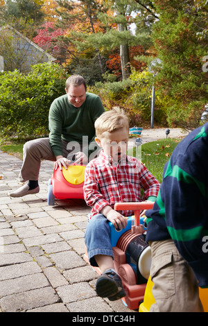 Vater und junge Söhne spielen auf Spielzeugautos im Garten Stockfoto