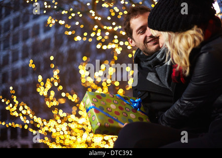 Junges Paar Austausch von Geschenken neben outdoor Weihnachtslichter Stockfoto