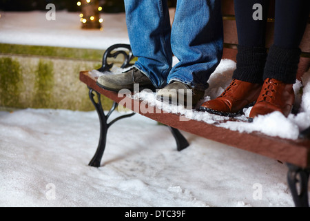 Die Beine des jungen Paares auf Schnee stehen bedeckt Parkbank Stockfoto