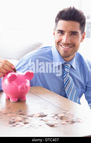 Gut aussehend Geschäftsmann, Münzen in die Piggy Bank Blick in die Kamera Stockfoto