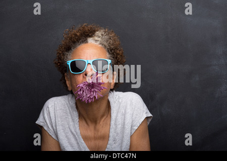 Studioportrait senior Frau mit Blume im Mund Stockfoto