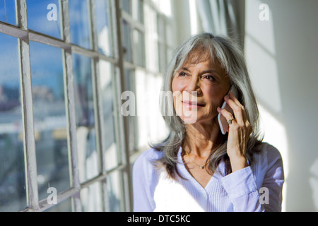 Ältere Frau Blick aus Fenster während Smartphone verwenden Stockfoto