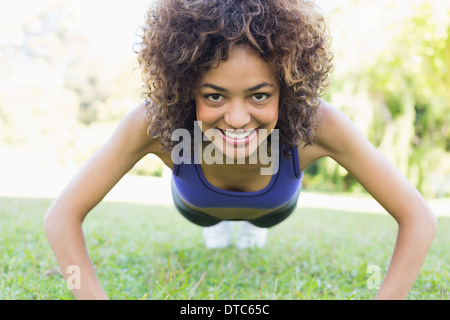 Lächelnde Frau doing Push-ups im Park Stockfoto